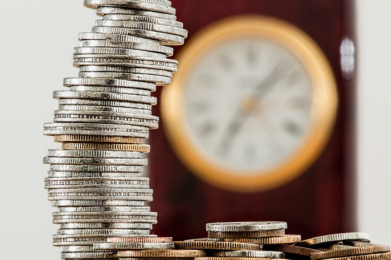 Services-02 A close-up image of stacked coins with a blurred clock, symbolizing time and money relationship.