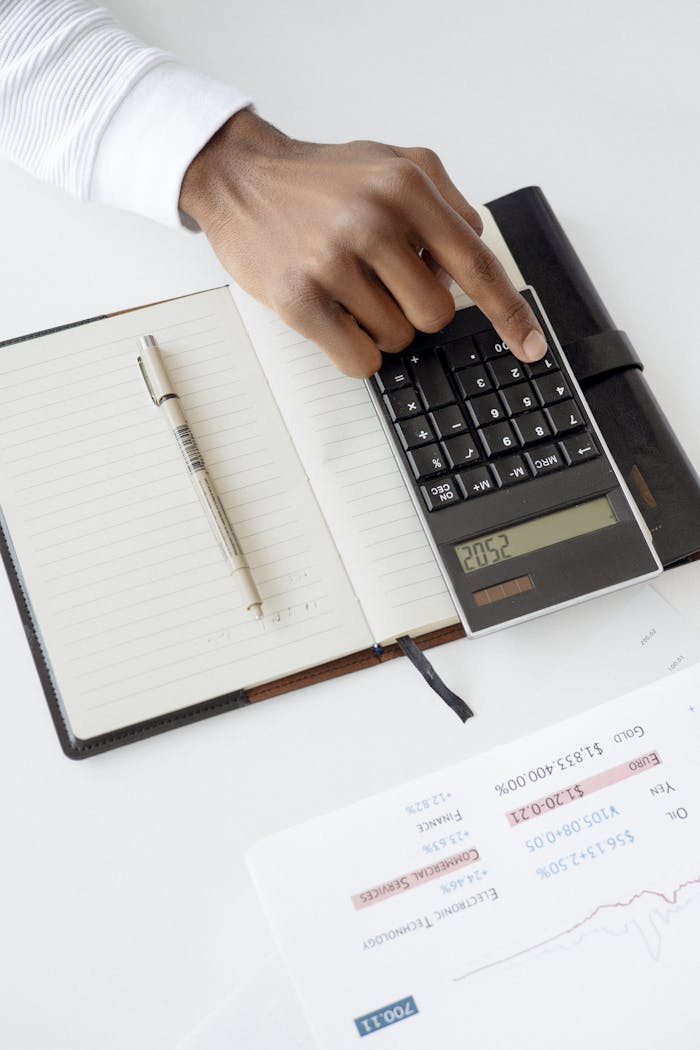 Services-03 A hand using a calculator with financial documents and notebook, depicting an office setup for financial analysis.